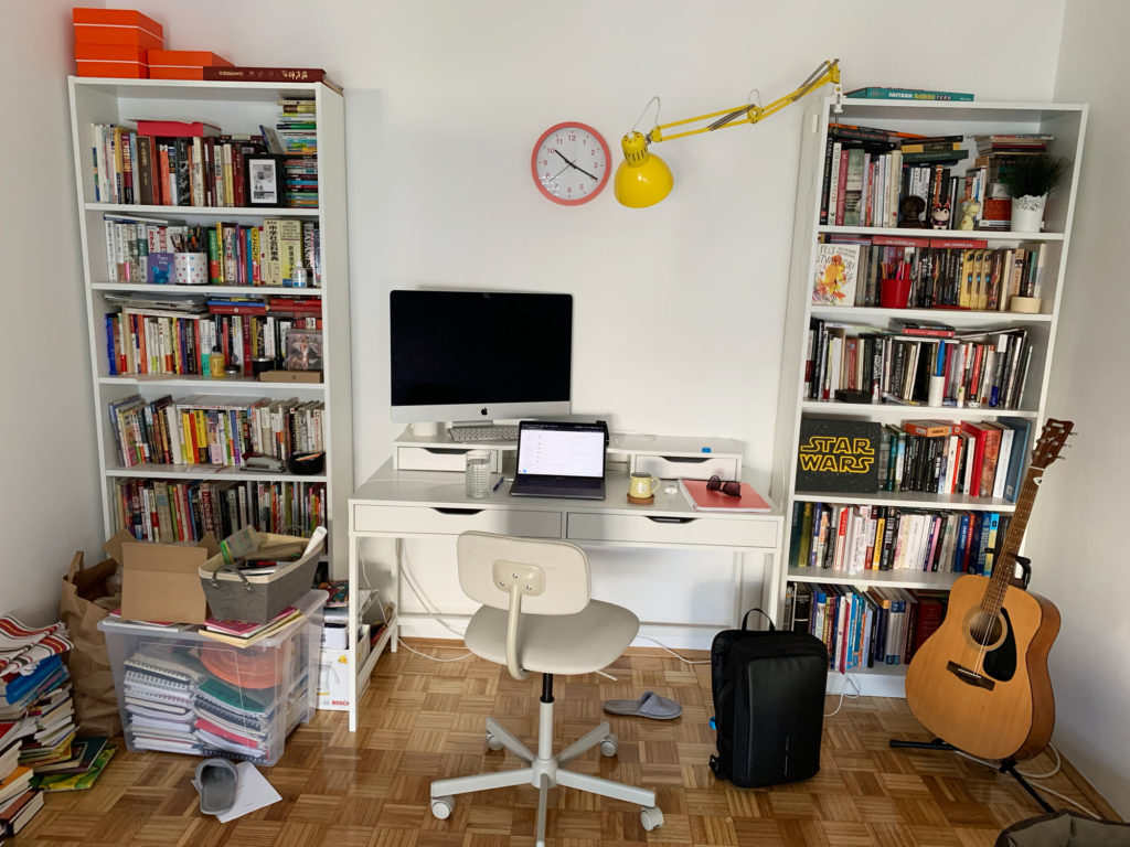 An image of a FishingBooker teammate's work from home space including a computer, bookshelves, and a guitar